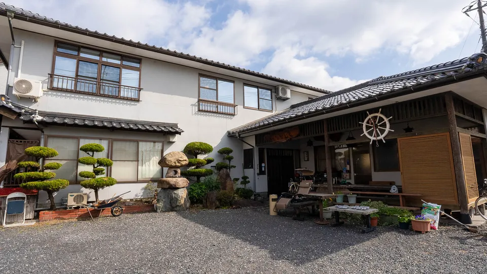 白壁に瓦屋根、松の庭と船の舵輪が飾られた、なかむらの外観。
